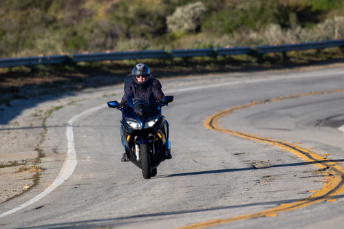 Free A man in a helmet rides a motorcycle on a winding road in a sunlit, rural setting. Stock Photo