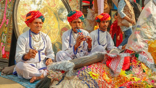 Indian Men in Traditional Clothing Sitting Crossed-Legged and Playing the Flute 
