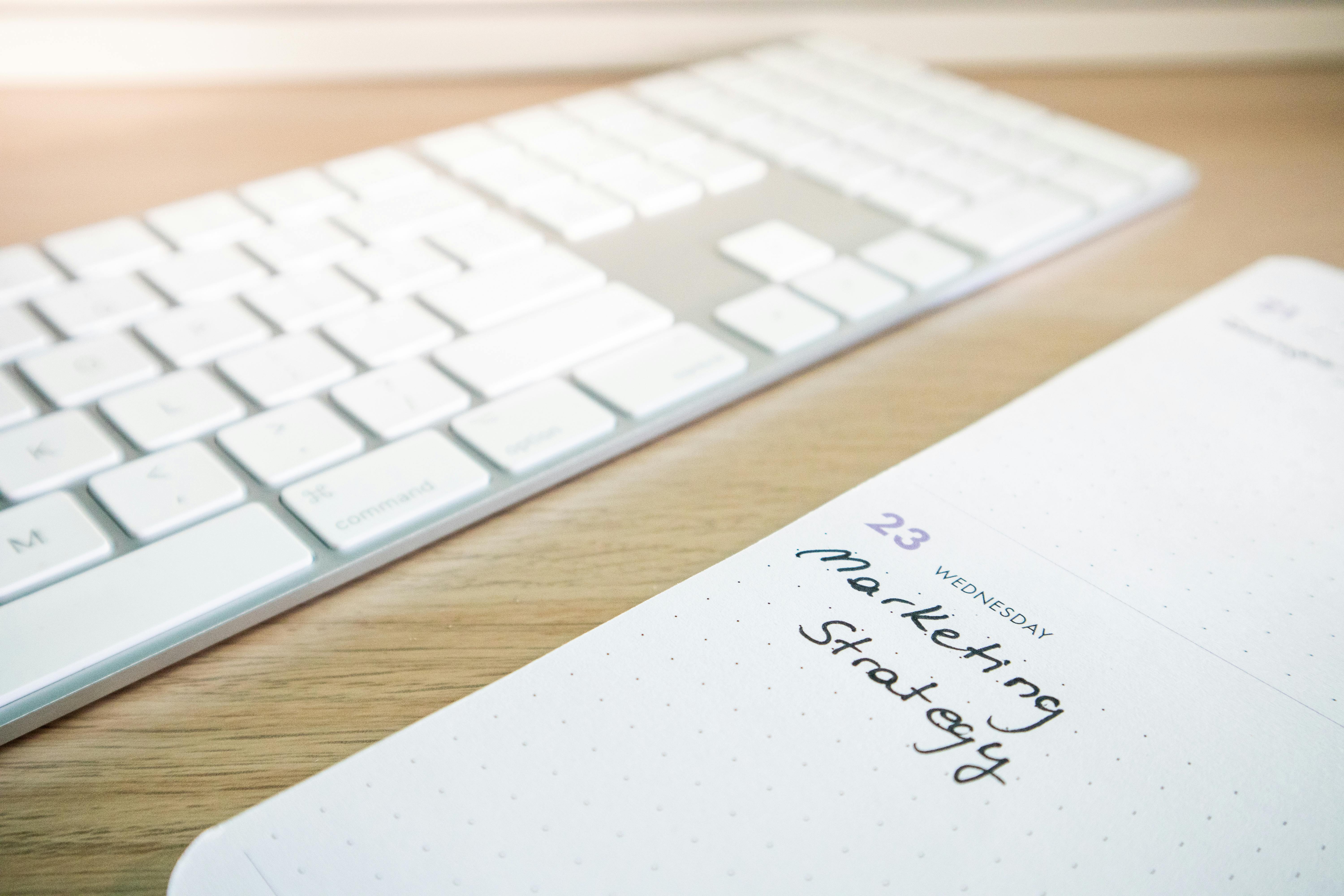 Notebook with marketing strategy note alongside a keyboard on a wooden desk.