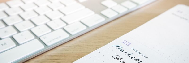 Notebook with marketing strategy note alongside a keyboard on a wooden desk.