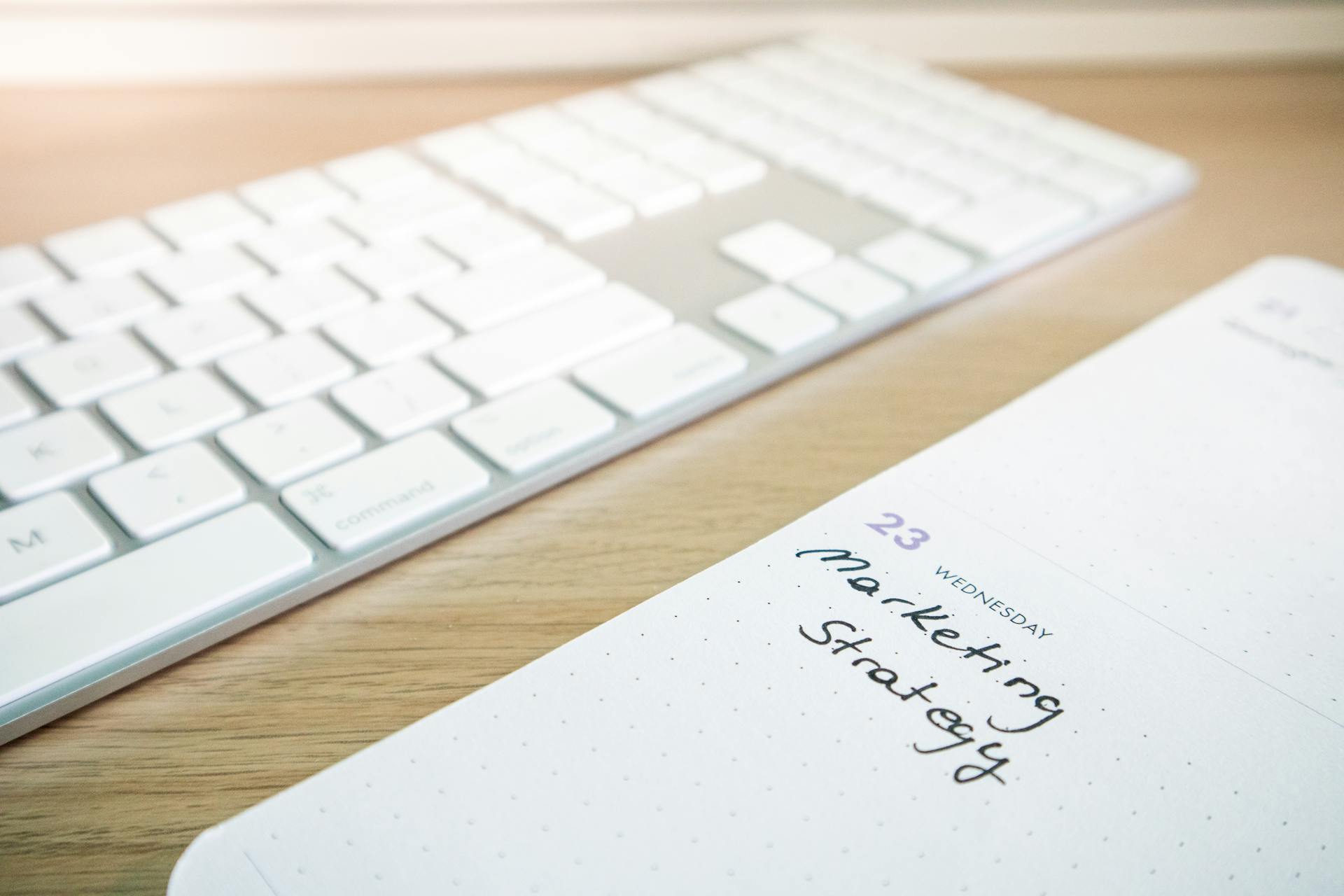 Notebook with marketing strategy note alongside a keyboard on a wooden desk.