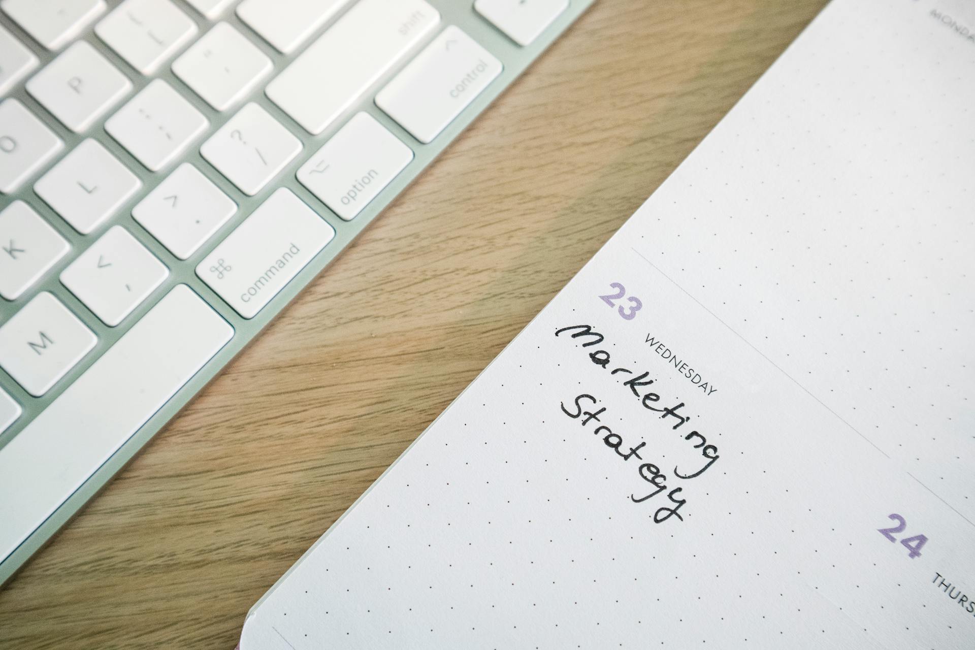 Close-up of a desk with a keyboard and a calendar open to a marketing strategy note.