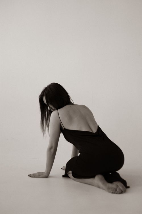 Free Artistic black and white photo of a woman in a backless dress crouching gracefully. Stock Photo