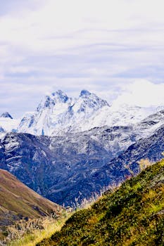 Snow-capped mountains rise under a cloudy sky, showcasing nature's grandeur.