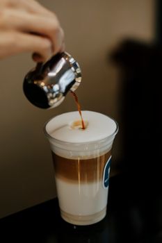Barista pouring espresso into a latte macchiato in a café setting. Captured in Baku, Azerbaijan.