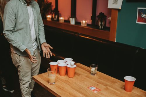 Free Casual beer pong game at a bar with a man standing beside a table with cups and ball. Stock Photo
