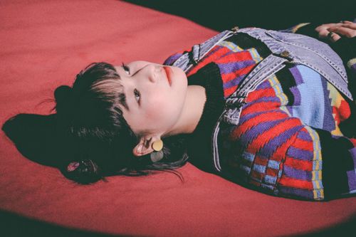 Free An artistic shot of a teenager in a colorful sweater lying on a red floor indoors. Stock Photo