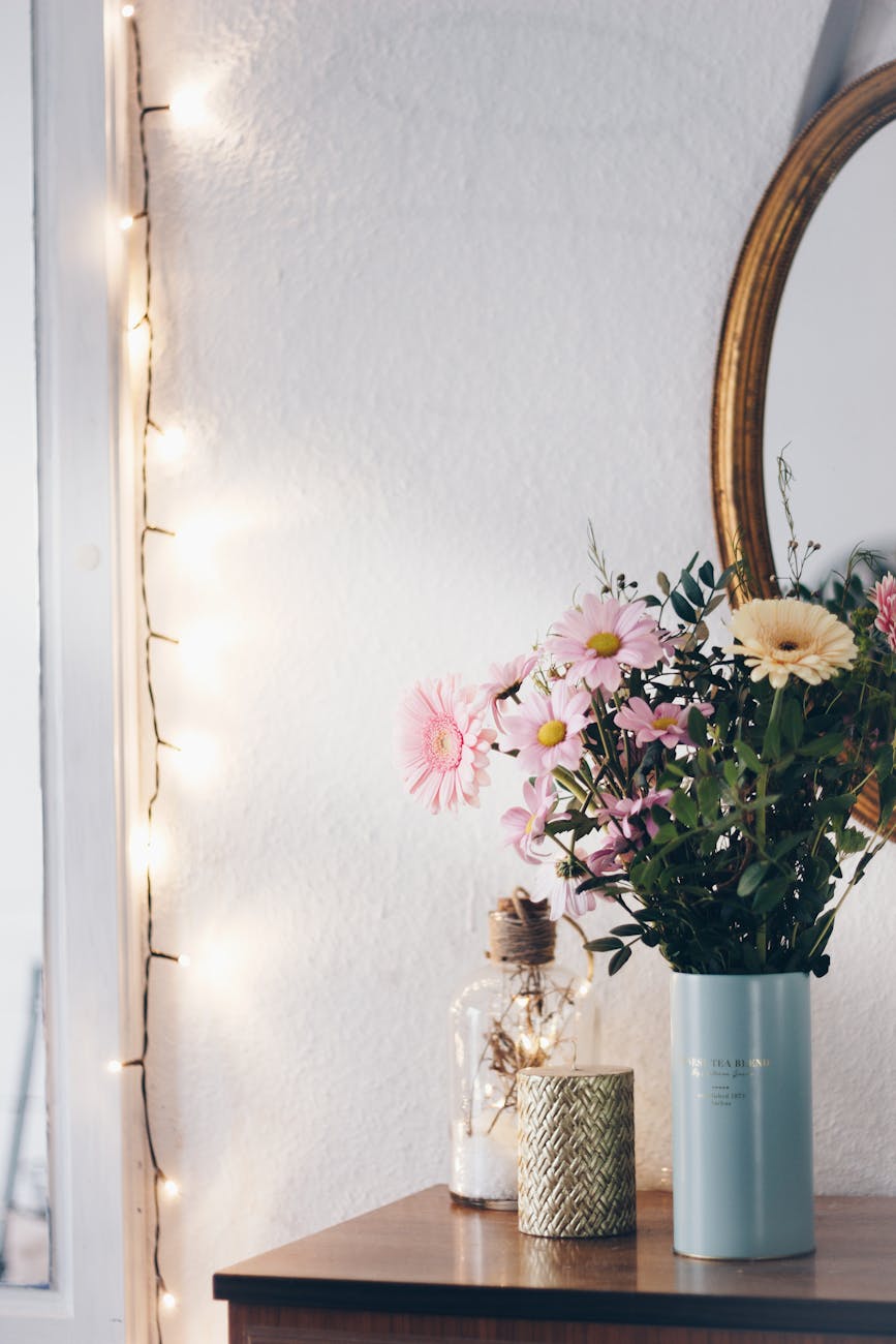A cozy interior featuring a floral arrangement in a vase, with string lights and a mirror creating a warm atmosphere.