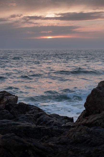 Beautiful sunset over a calm sea with rocks in the foreground, perfect for serene themes.