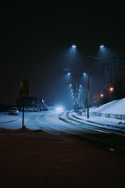 Free A tranquil snowy urban street illuminated by streetlights during nighttime. Stock Photo