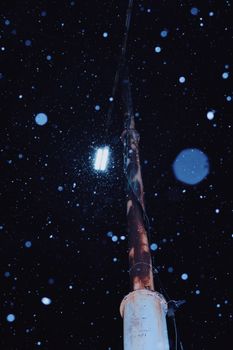 A streetlight illuminates falling snowflakes on a cold winter night.