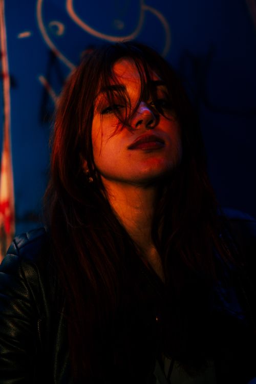 Free Dramatic nighttime portrait of a woman with eyes closed against a colorful urban background. Stock Photo