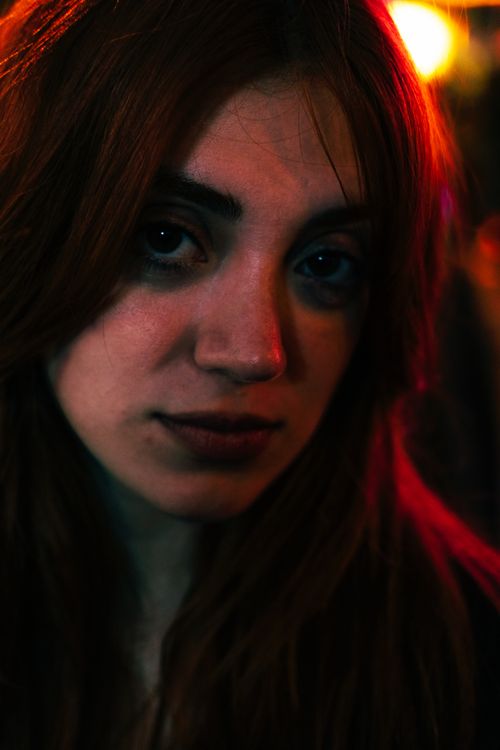 Free Intimate close-up portrait of a woman with red hair and black hair highlights, featuring moody lighting and a thoughtful expression. Stock Photo