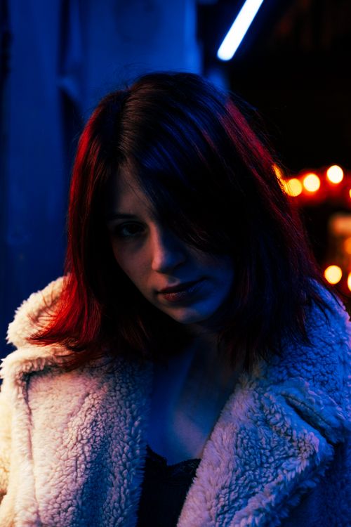Free Portrait of a woman in a cozy coat illuminated by city lights at night. Stock Photo
