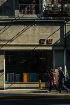 City street with pedestrians walking past a storefront with suitcases, capturing urban life.
