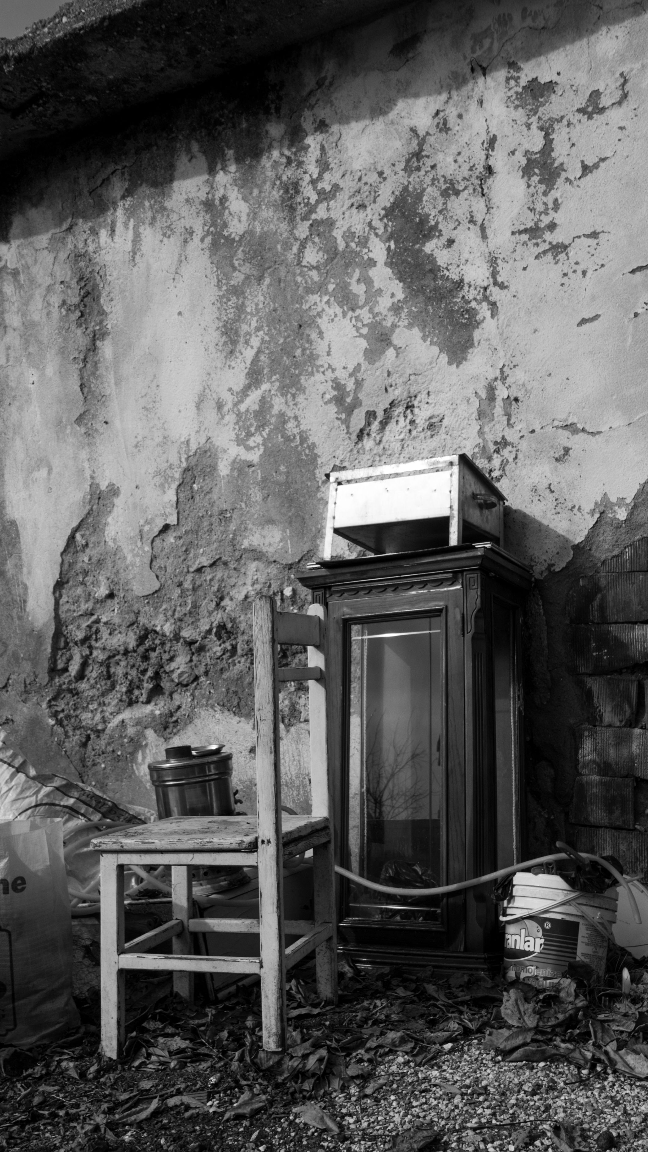 Black and white image of aged furniture and objects against a cracked wall, evoking nostalgia.