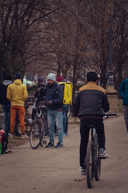 Free Men on bicycles in a busy Bucharest park during autumn, with Glovo delivery visible. Stock Photo