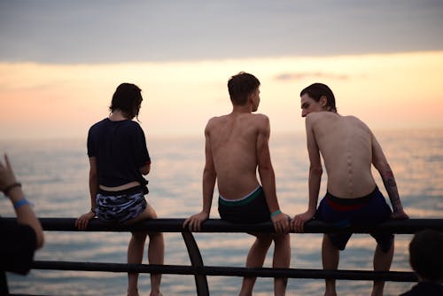 A Group of Young People Sitting the Railing of a Pier at Sunset 