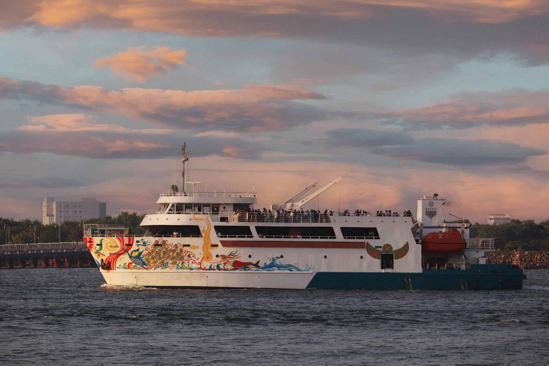 A vibrant cruise ship sails through a scenic harbor at sunset with artistic hull designs.