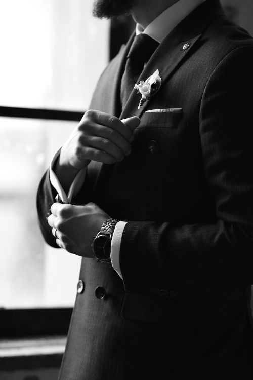 Free Black and white portrait of a man in a suit, adjusting with floral boutonniere and wristwatch. Stock Photo