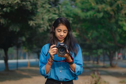 Free A young woman holds a camera in a sunny park setting, capturing moments. Stock Photo