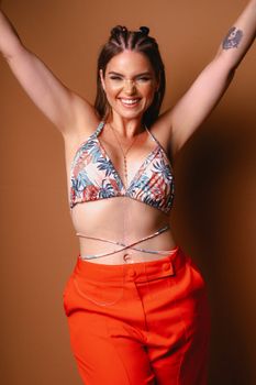 Smiling woman in a floral top and orange pants in a studio setting.