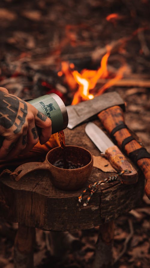 Man Pouring Coffee to Cup by Campfire