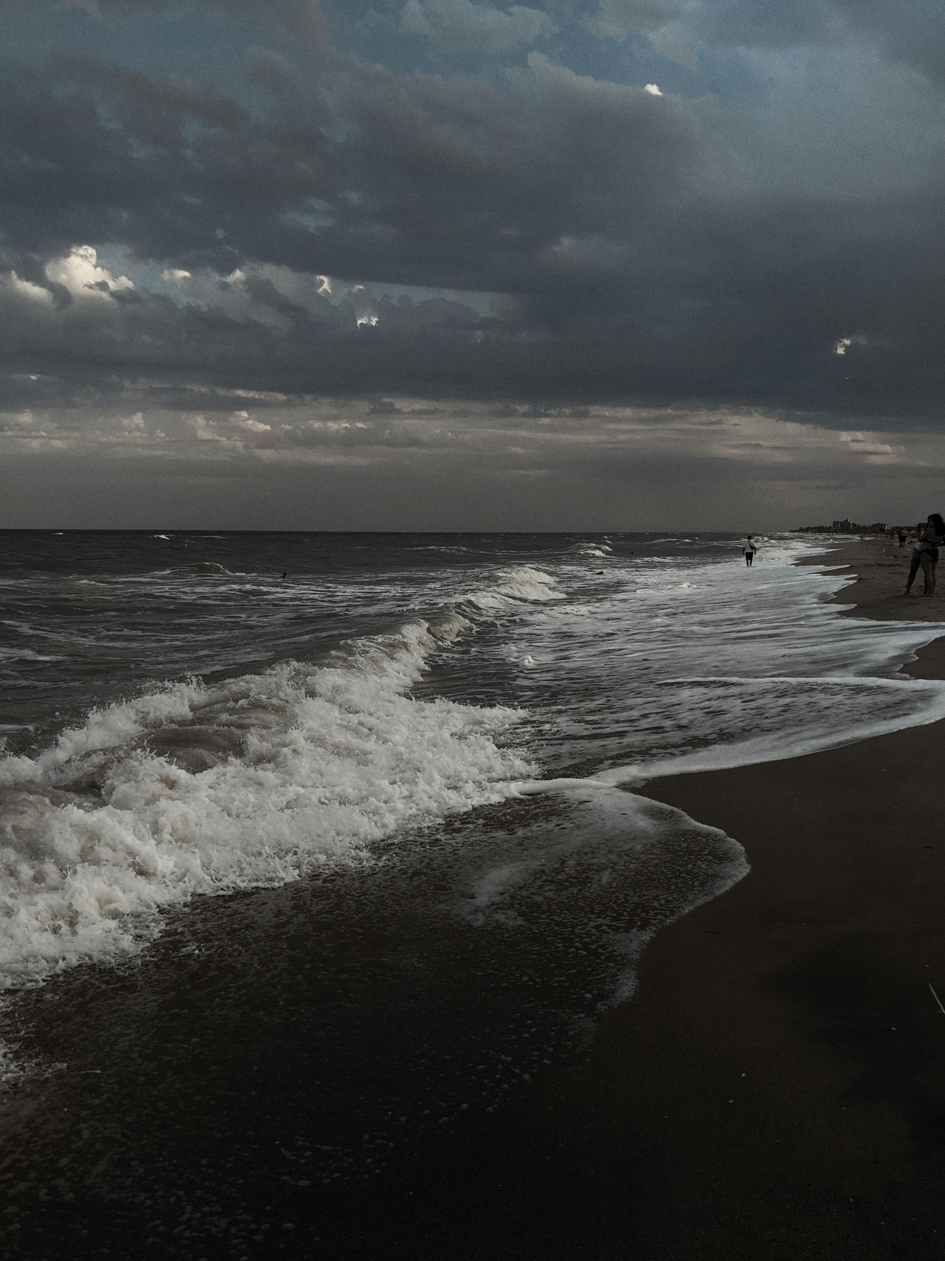 A dark and moody ocean scene at dusk, featuring crashing waves and a cloudy sky.