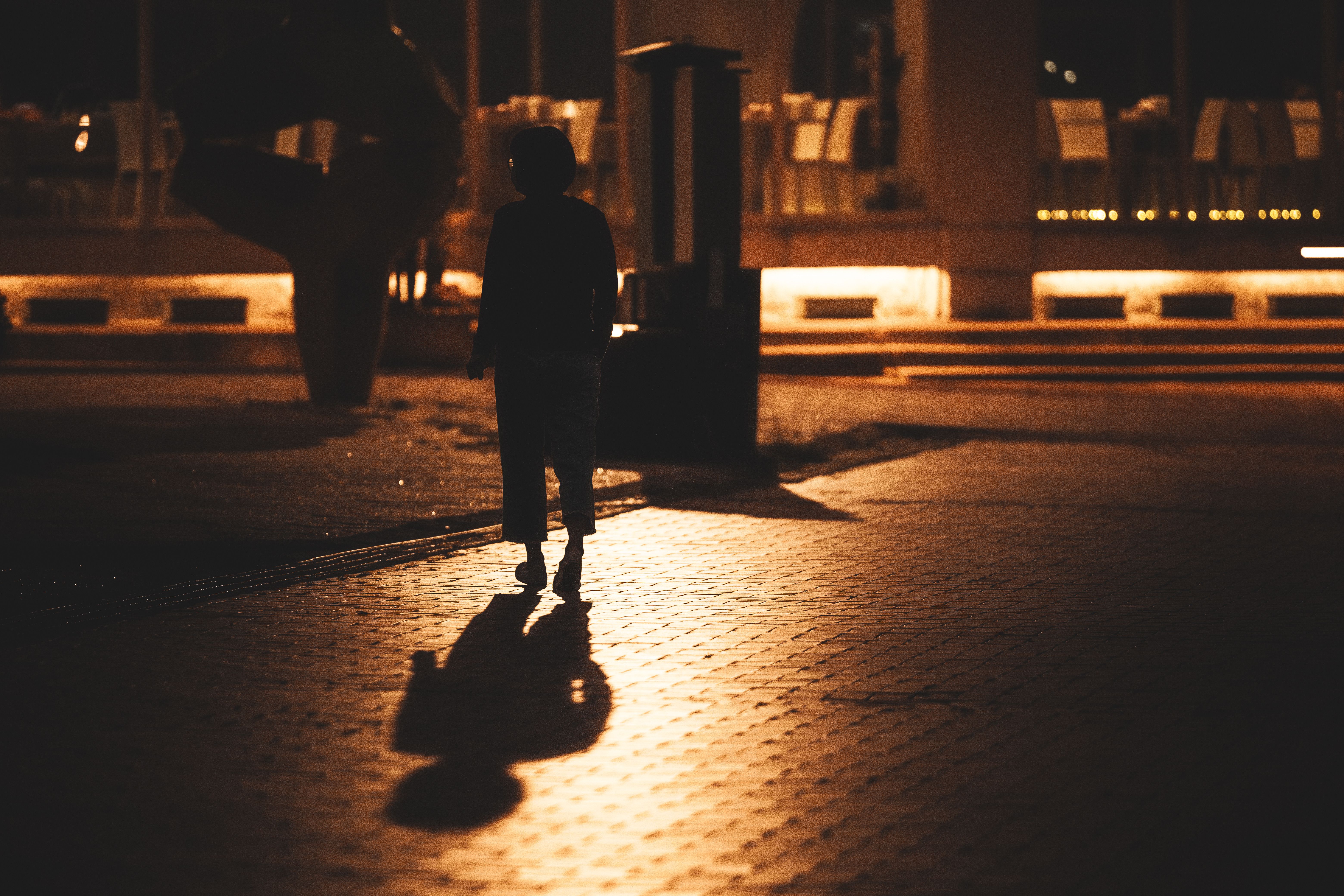 Gece vakti az ışıklı şehir kaldırımında yürüyen bir kadının silüeti.