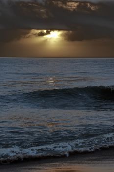 Calm ocean waves under a dramatic twilight sky with clouds breaking sunlight.