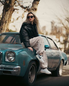 Fashionable woman sitting on a classic car in a stylish outdoor shoot.