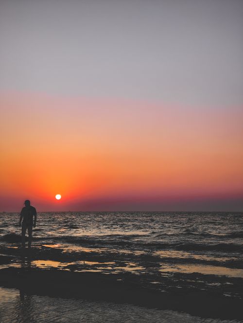Free A lone silhouette walks along a serene seaside during a vibrant sunset. Stock Photo