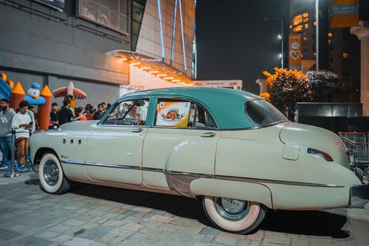 Classic green vintage car showcased at a nighttime auto exhibition with a bustling crowd.