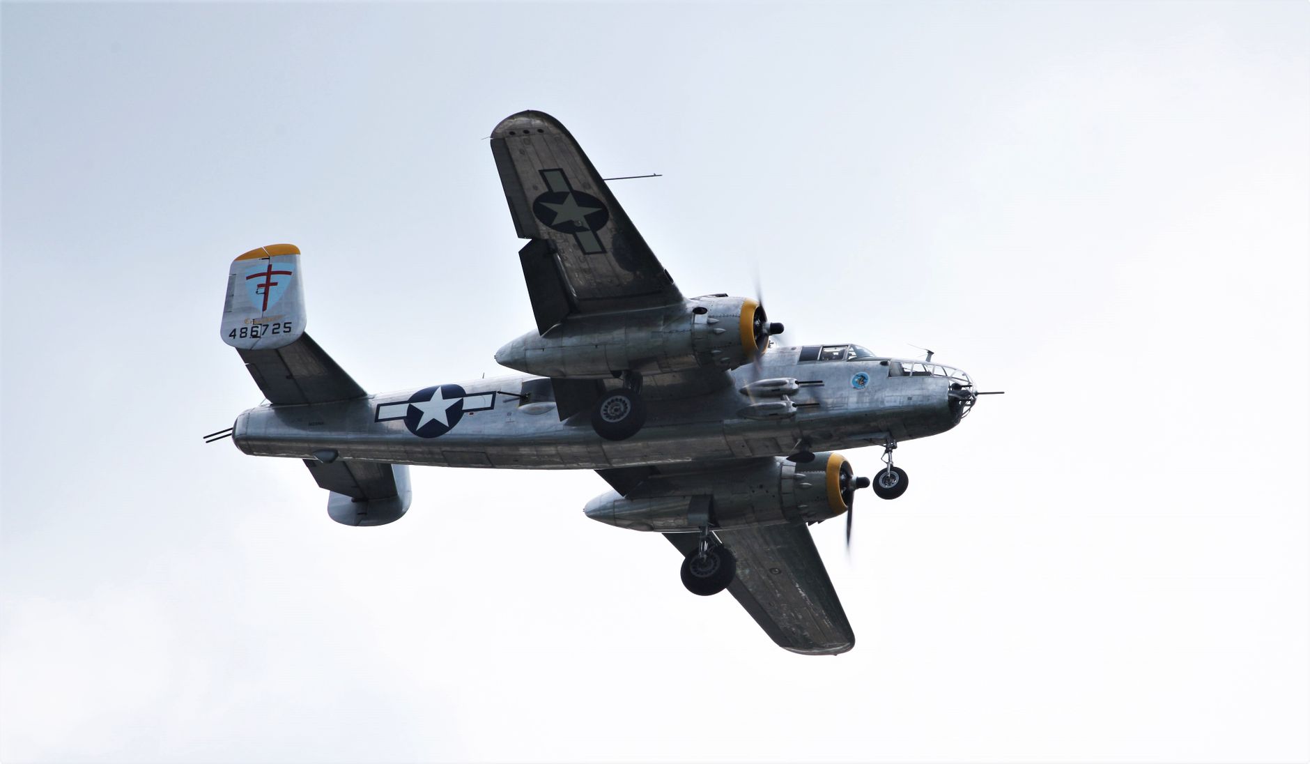 A classic B-25 Mitchell bomber aircraft captured flying in a clear sky during daylight.