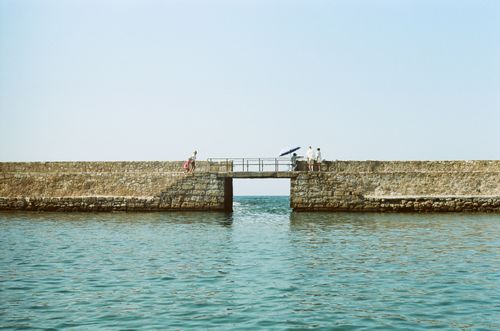Free A serene view of a stone pier with people enjoying a sunny day by the sea. Stock Photo