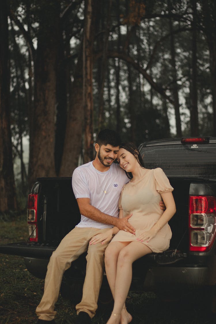 Happy Pregnant Couple Sitting In Car Trunk