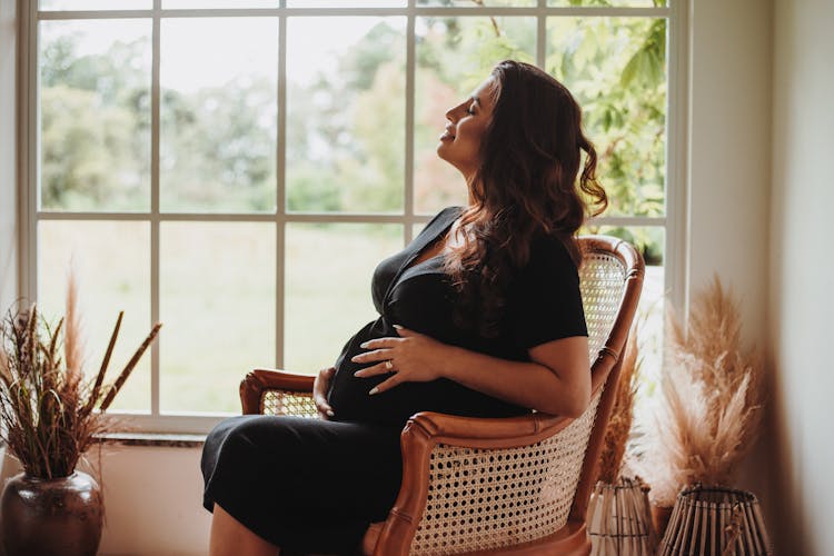 Happy Pregnant Woman Sitting In Chair Near Window