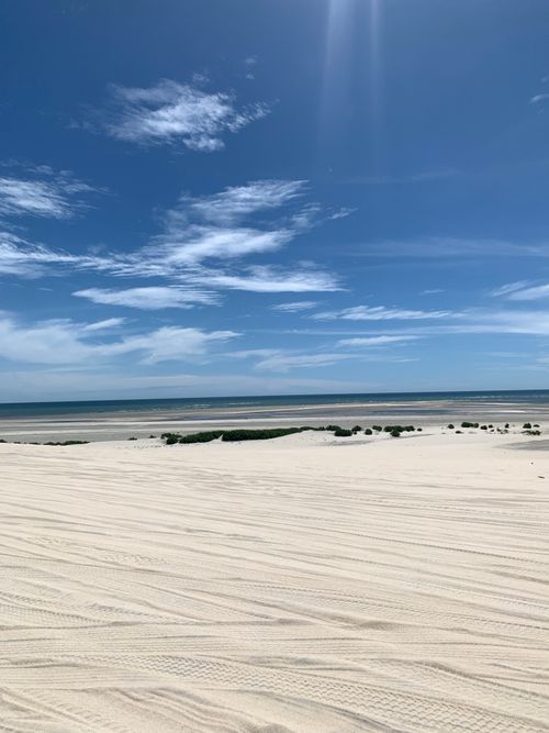 Free Tranquil beach scene with white sand dunes under a vibrant blue sky, ideal for travel and vacation imagery. Stock Photo
