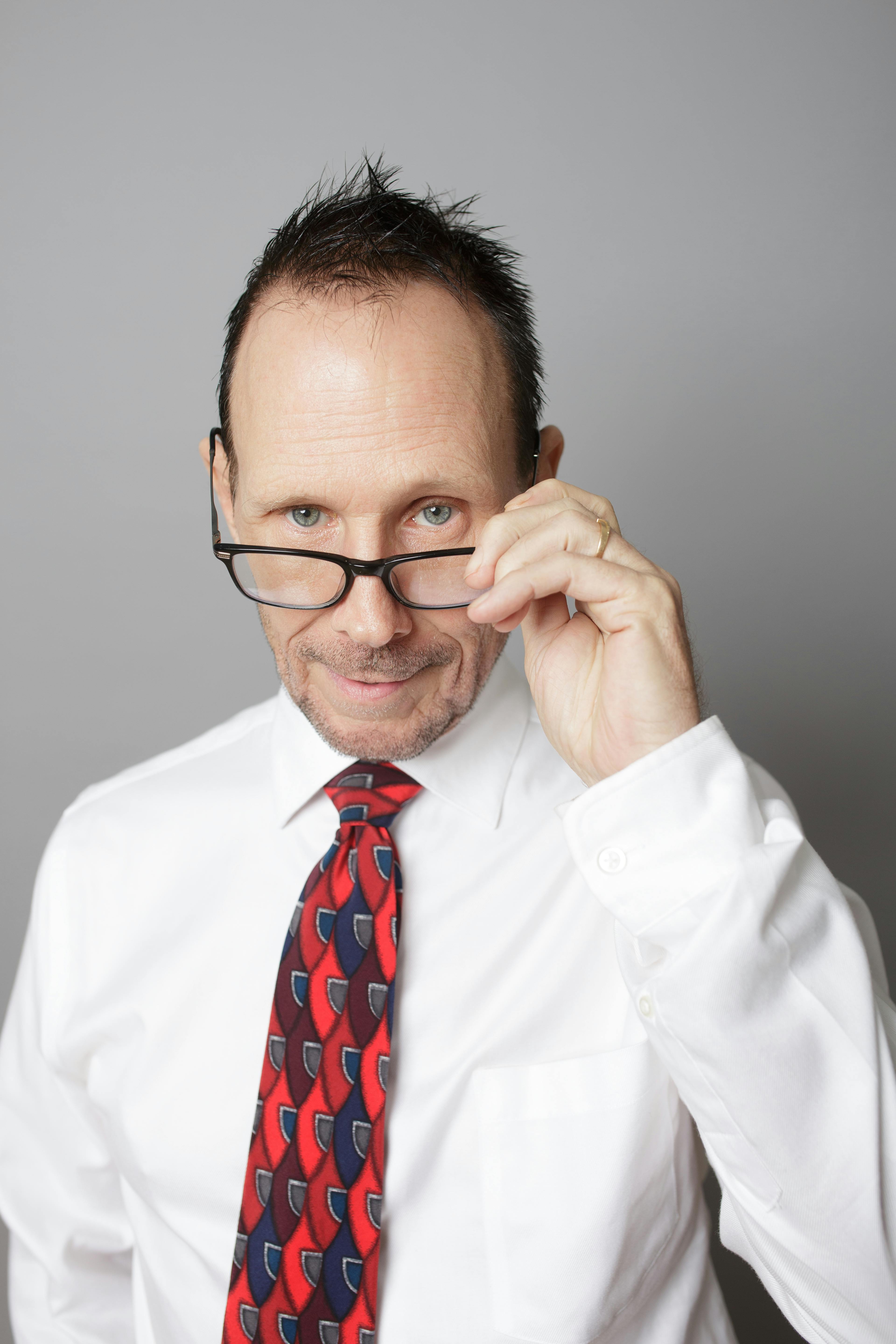 Professional man in white shirt with colorful tie adjusting glasses, exuding confidence.