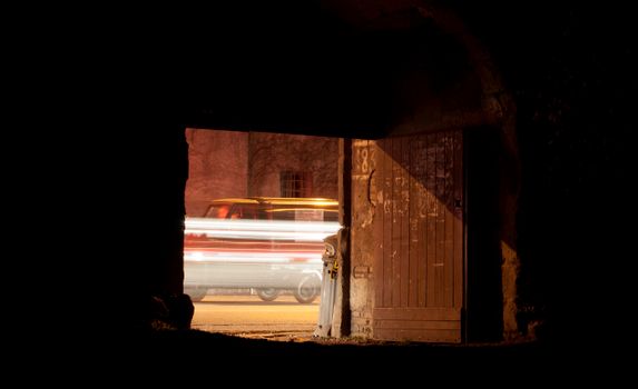 A car's light streaks captured in a long exposure through a dark doorway at night.