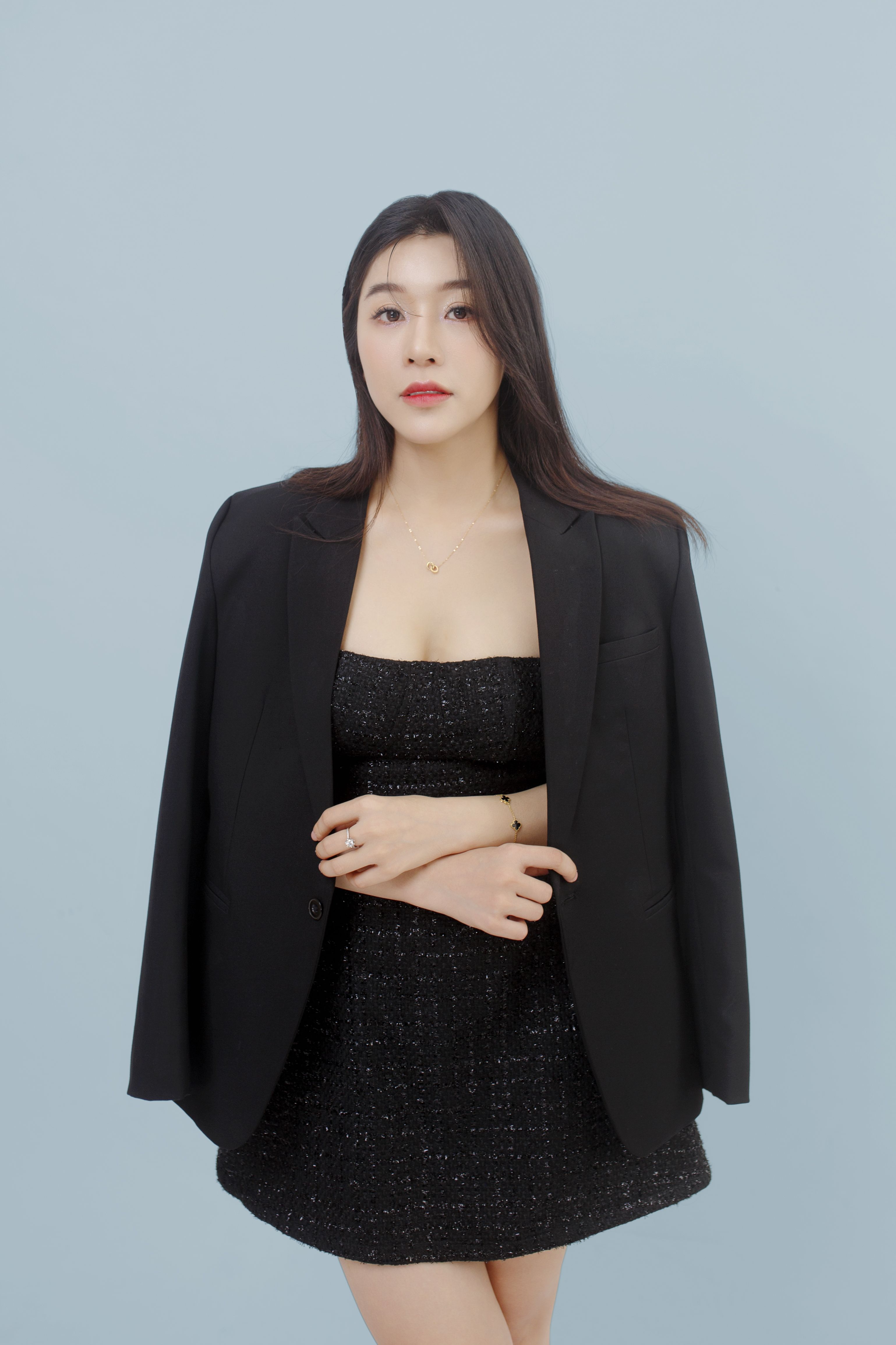 Portrait of a stylish Asian woman wearing a black outfit and blazer against a gray background.