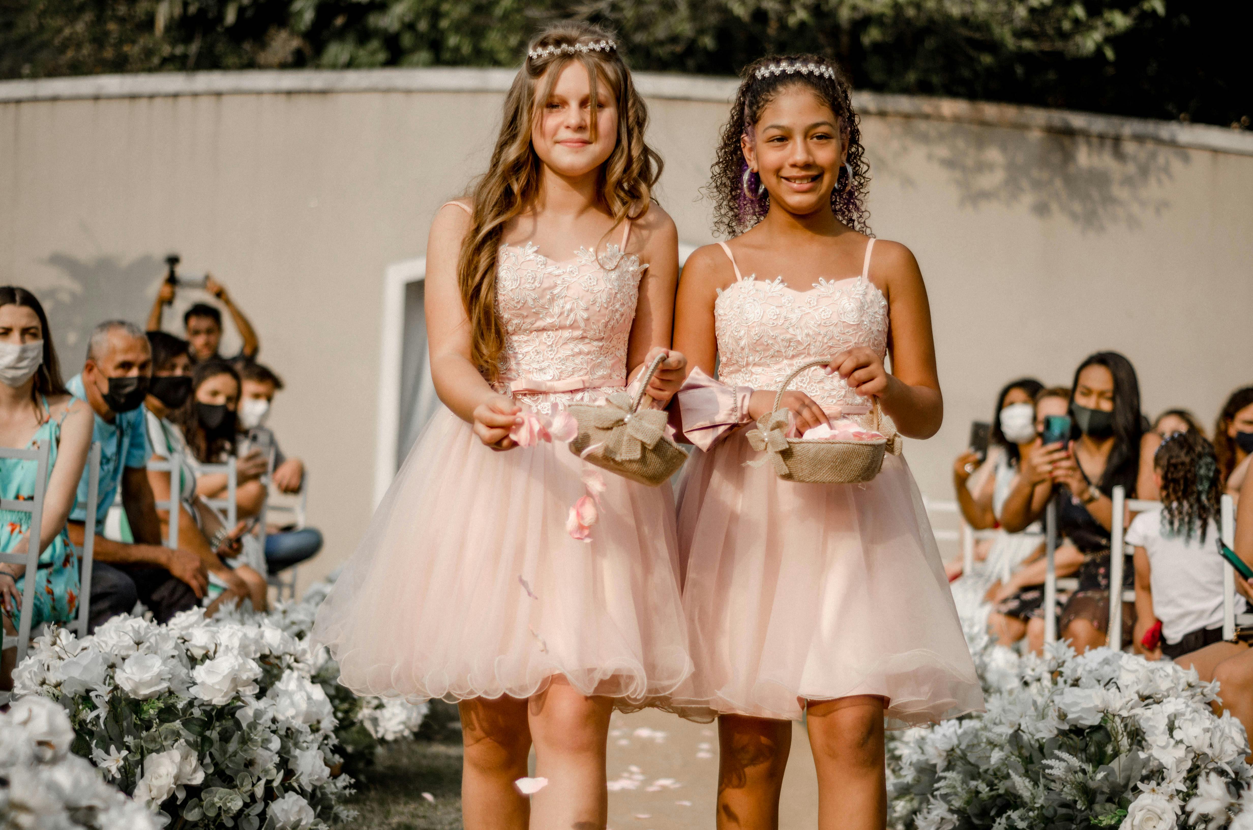 Two adorable flower girls in pink dresses walk down the aisle at an outdoor wedding.