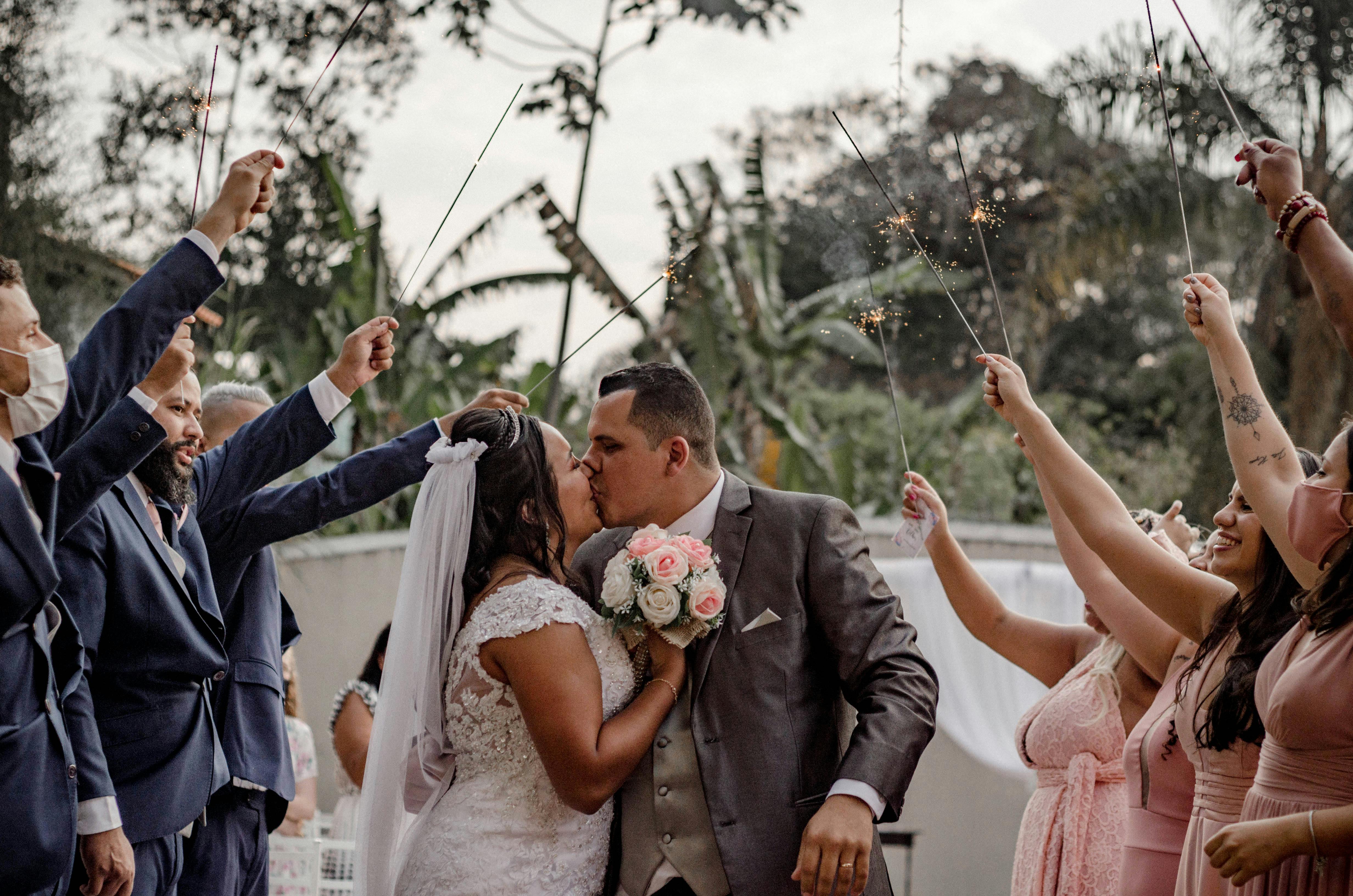 Bride and groom kissing under sparklers held by guests in an enchanting outdoor setting.