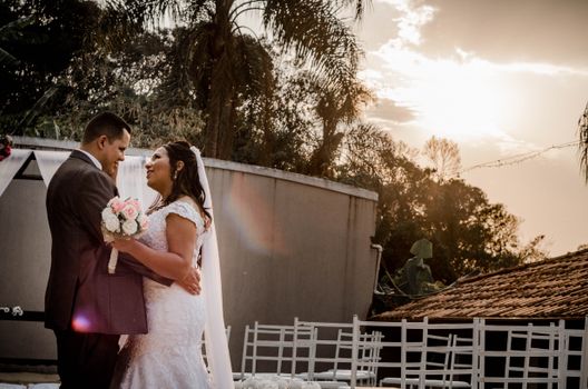 Newlywed couple embracing and smiling under the warm outdoor sunset, celebrating their special day.