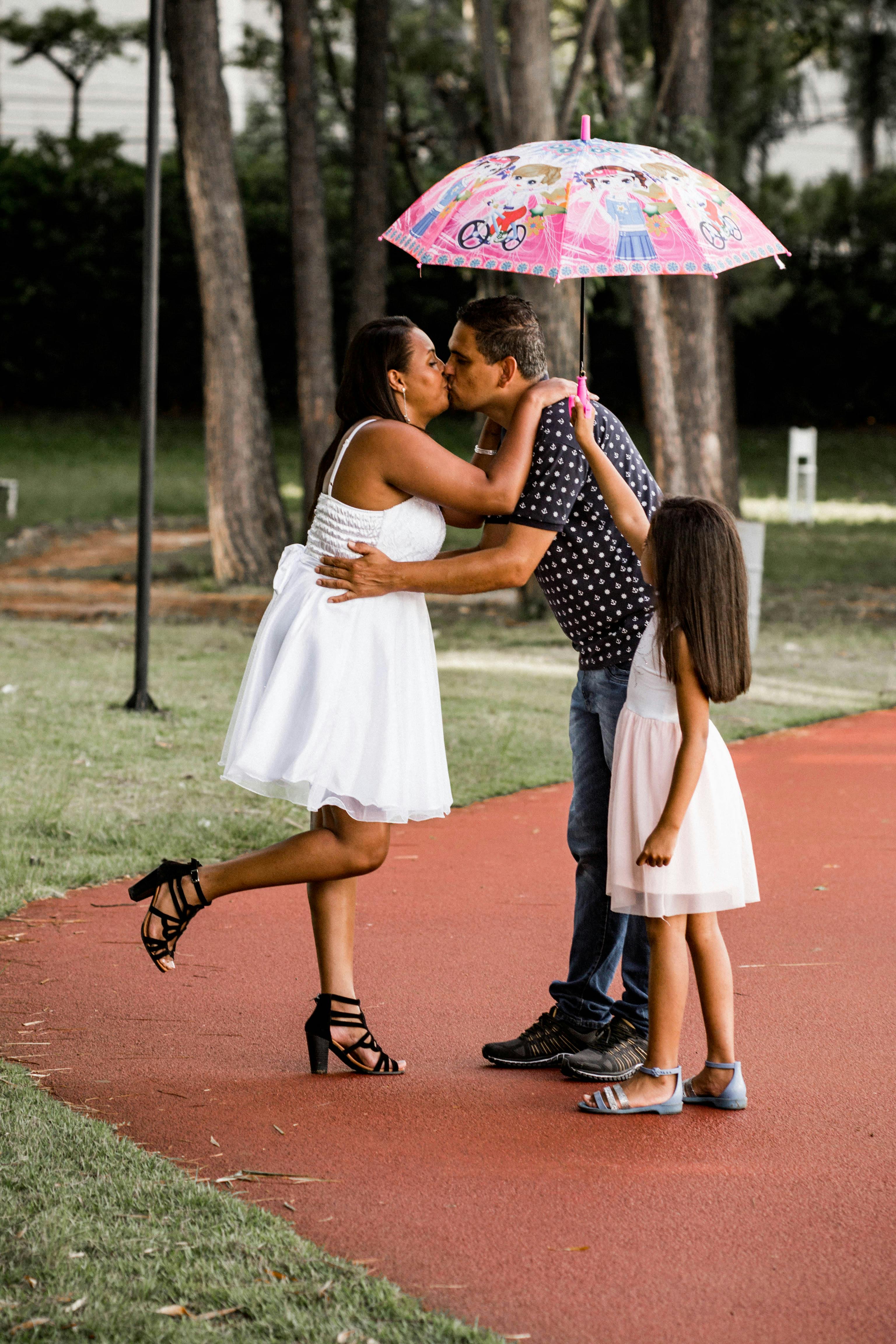 Family moment with parents kissing under an umbrella while daughter looks on.