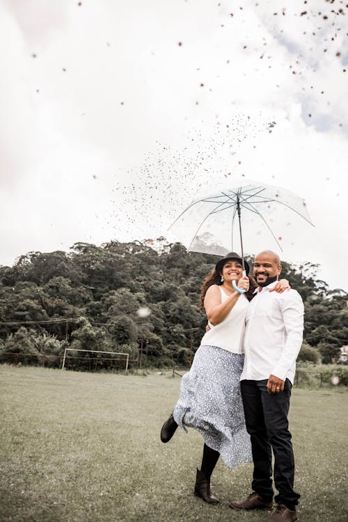 A Happy Couple Standing Outdoors under an Umbrella 