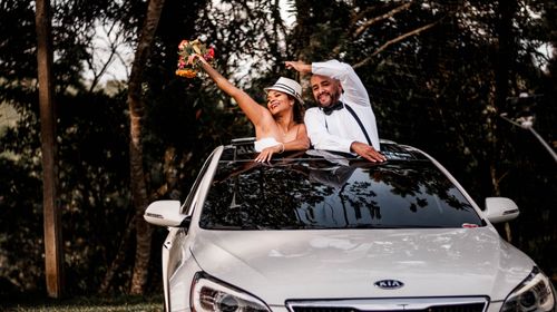 Free Happy couple celebrating their wedding day, popping out of a car's sunroof with flowers. Stock Photo