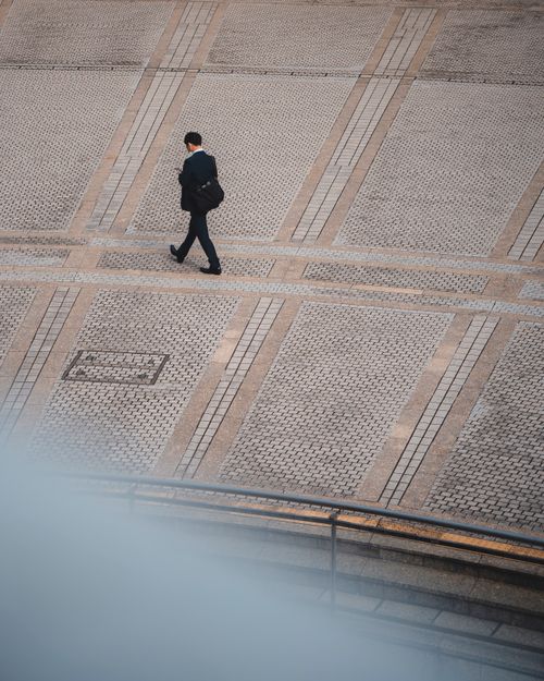 Free A lone businessman dressed in a suit walks across a patterned pavement from a high angle view. Stock Photo