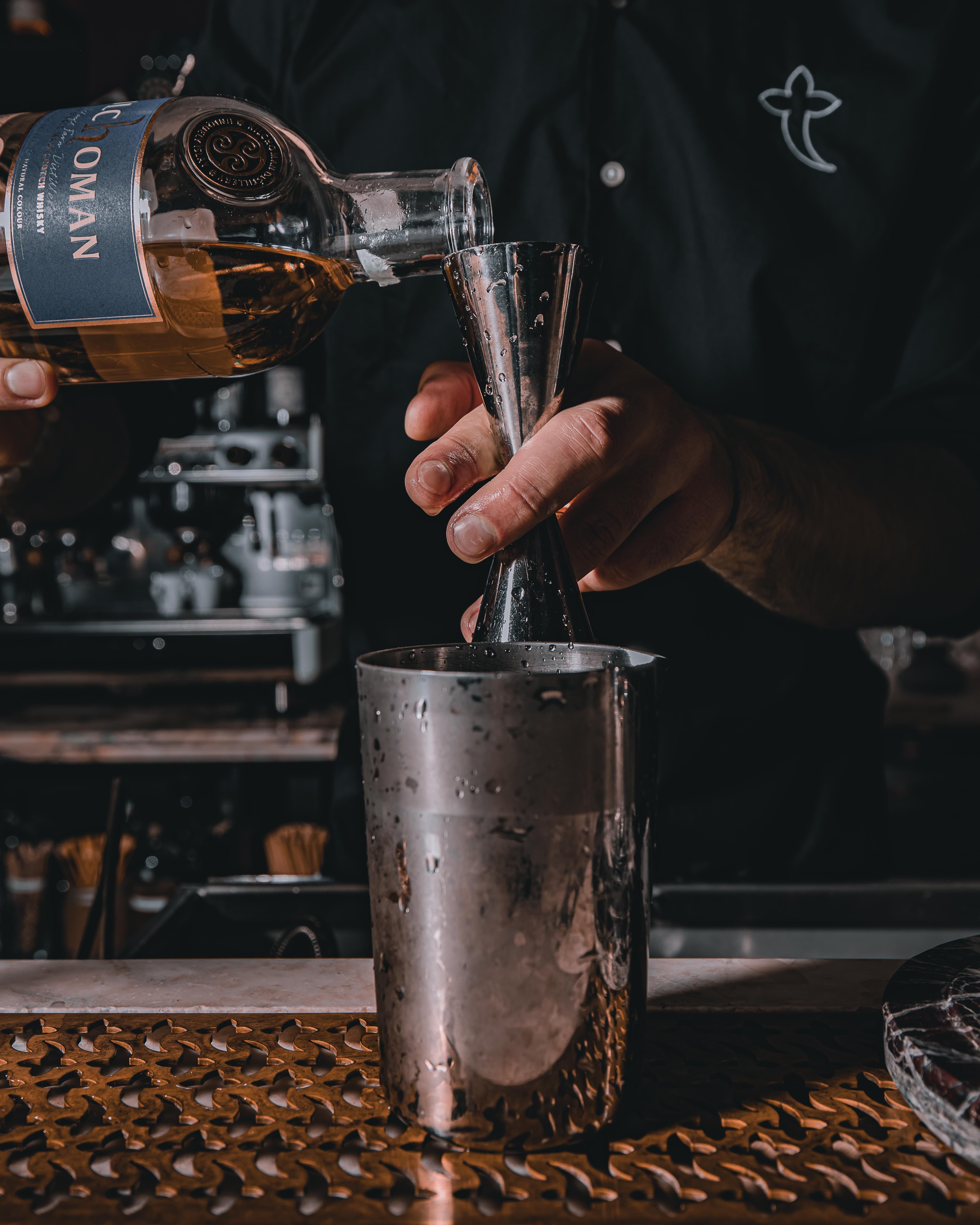 Bartender pouring whiskey into a jigger at a bar counter, showcasing skill and precision.