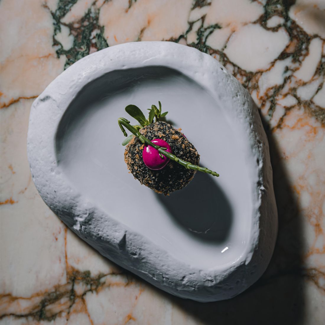 A close-up of a gourmet dessert on a stone plate with vibrant decoration.